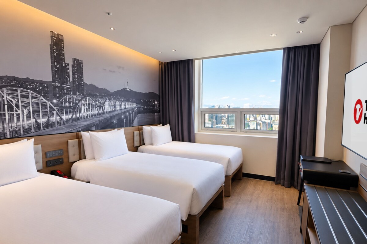 A hotel room with three beds, a cityscape mural, a large window with curtains, and a flat-screen TV.