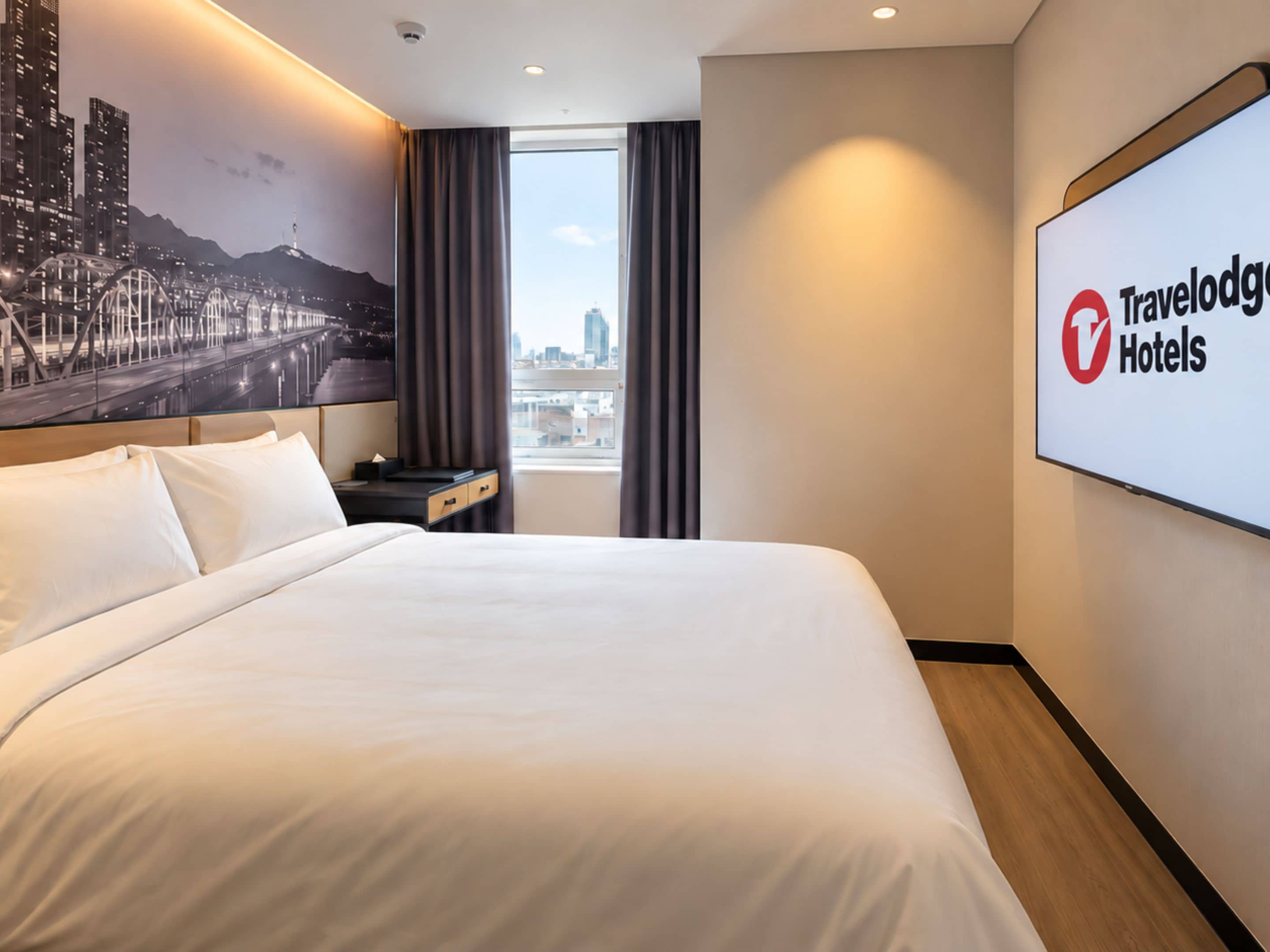 Ein Hotelzimmer mit einem großen Bett, einem Nachttisch, einem Fenster mit Vorhängen, einem Stadtbild-Wandbild und einem Schild von Travelodge Hotels.