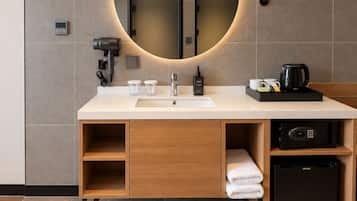 A modern bathroom with a white sink, a mirror, a hairdryer, a kettle, and a small refrigerator.