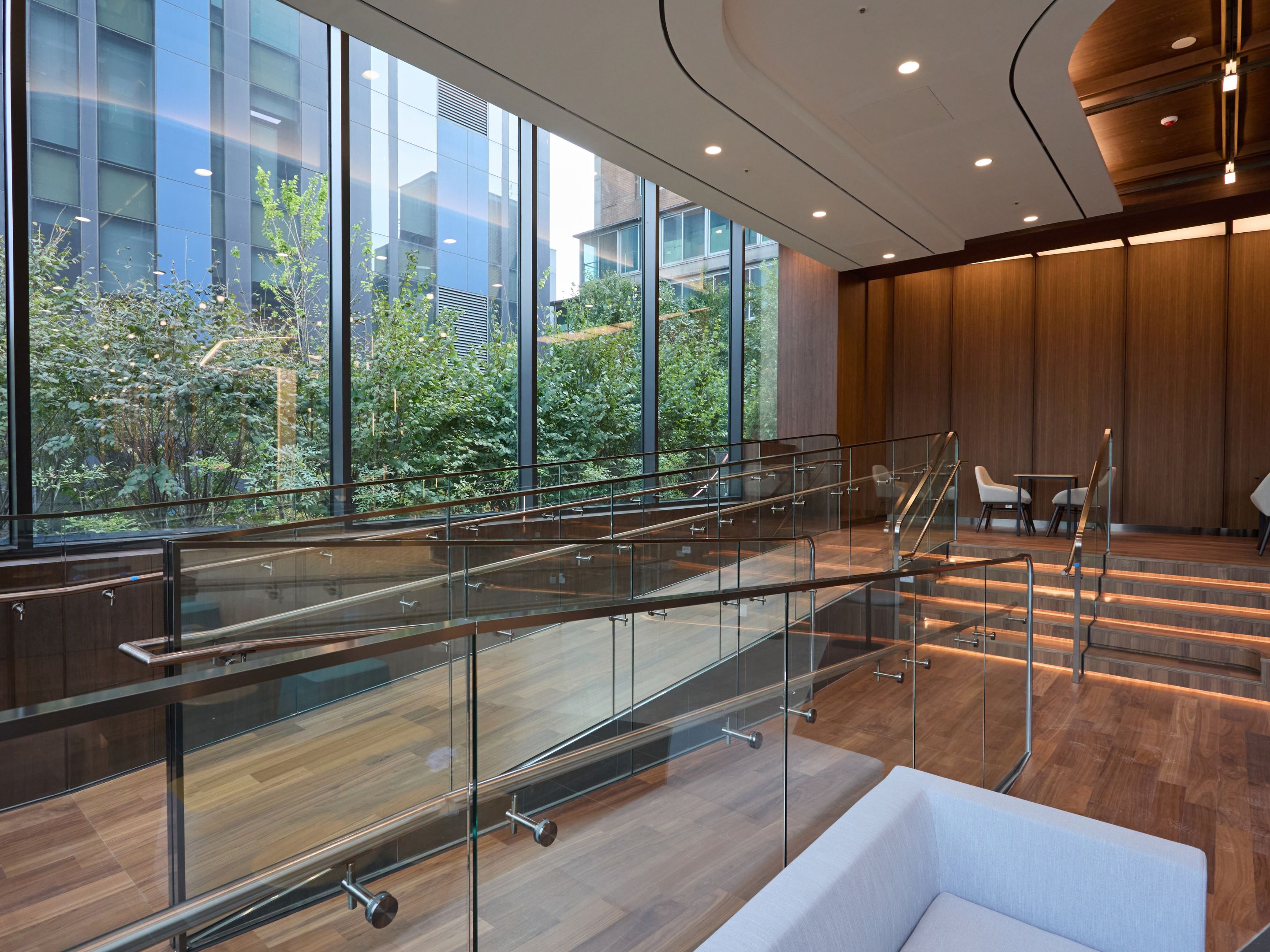 A modern interior with a glass railing, wooden flooring, and a view of greenery outside.