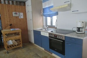 A kitchen with a built-in oven, a coffee maker, and a wooden wall with a thermostat. - Holiday apartment with 1 bedroom (Gunzenhausen)