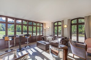 Un salon spacieux avec de grandes fenêtres, un ensemble de canapés, une table basse et un tabouret de bar.