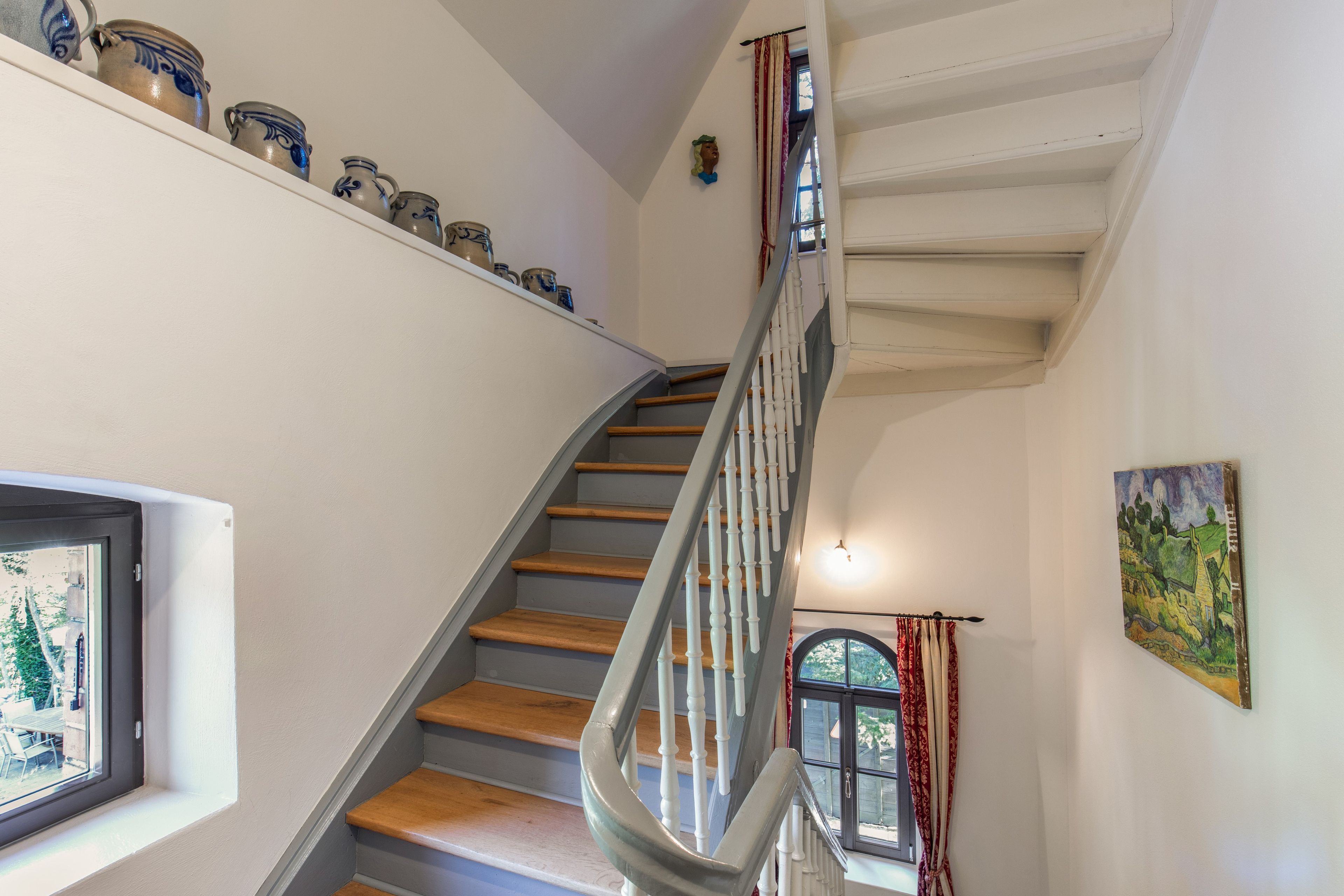 A staircase with a handrail, a window with a view of the outside, and a collection of ceramic pots on the wall.
