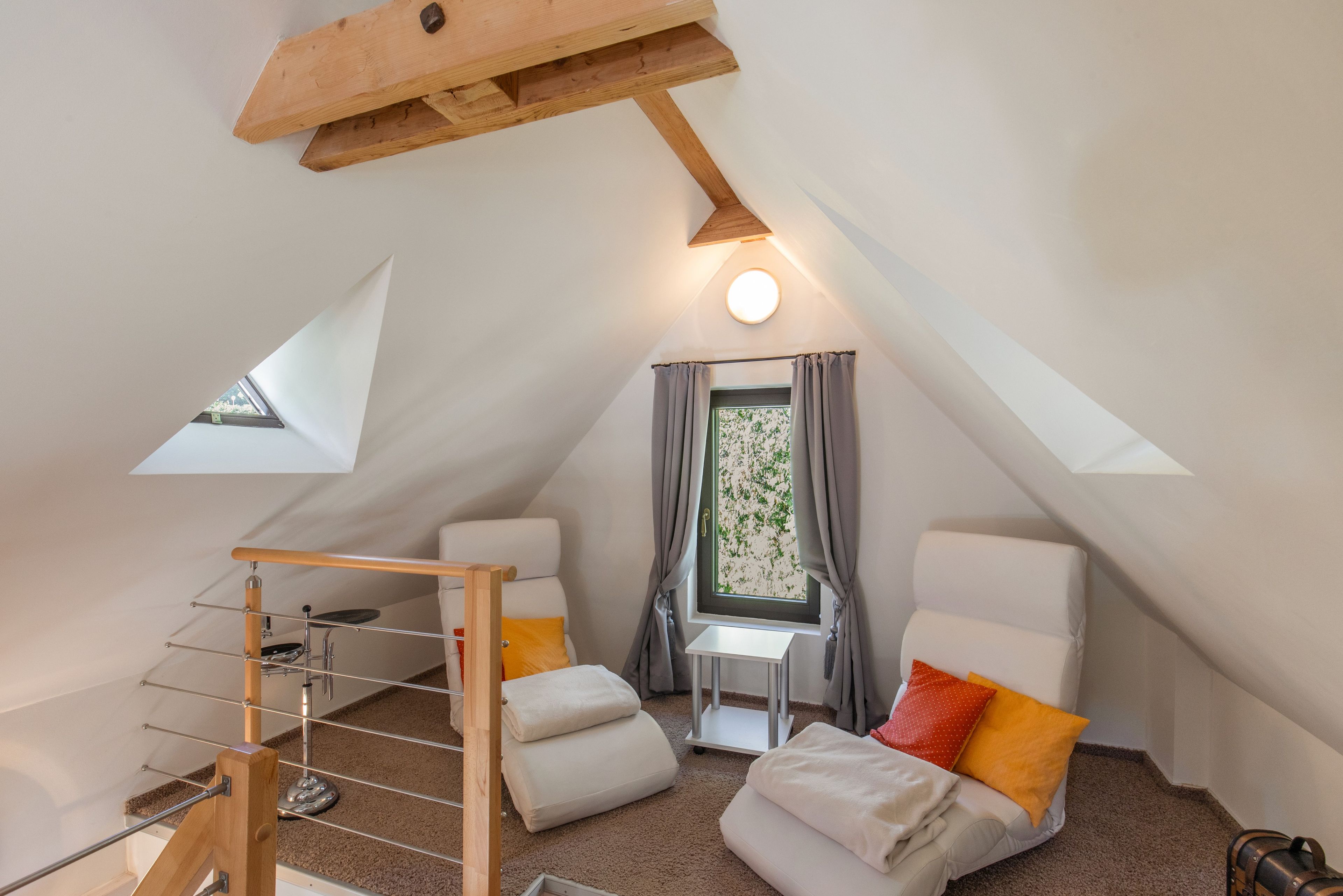 Ein gemütliches Schlafzimmer im Dachgeschoss mit geneigter Decke, einem kleinen Tisch, zwei Stühlen, einem Etagenbett und einem Fenster mit Vorhängen.