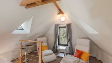 A cozy attic bedroom with a sloped ceiling, a small table, two chairs, a bunk bed, and a window with curtains.