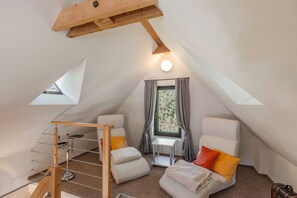 A cozy attic bedroom with a sloped ceiling, a small table, two chairs, a bunk bed, and a window with curtains.