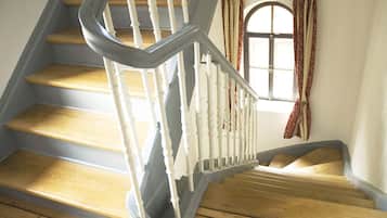 A wooden staircase with white balusters and a curved handrail, leading to a landing with a window and curtains.