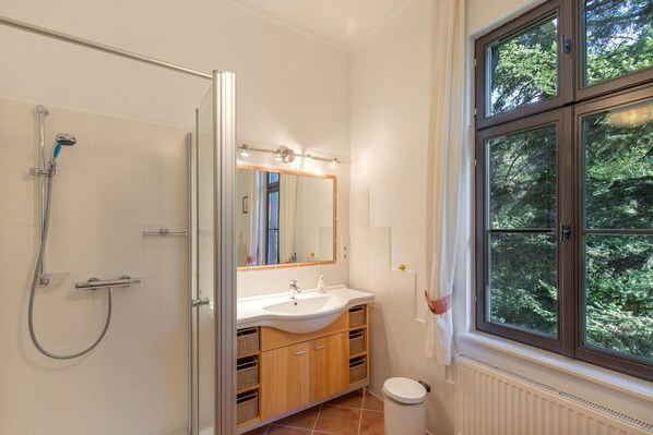 Une salle de bain avec une douche, un lavabo, un miroir et une fenêtre donnant sur des arbres.