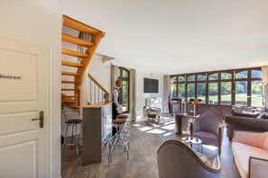 A spacious living area with a wooden staircase, a seating area with a sofa and chairs, and a large window providing a view of the outdoors.