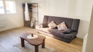 A living room with a sofa, a coffee table, a hanging coat rack, and a window. - Homerez - Studio Chauny (Chauny)