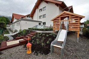 A residential area with a house, a wooden play structure, and a slide. - Bernstein Suite DUKE ALBRECHT (Oberstdorf)
