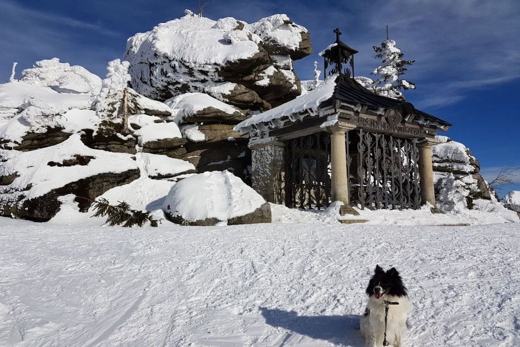 A snow-covered landscape with a rock formation and a small building with columns.