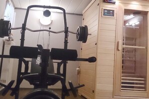 Une salle de sport équipée de matériel d’exercice, d’un sauna et d’une porte dotée d’un panneau de commande.