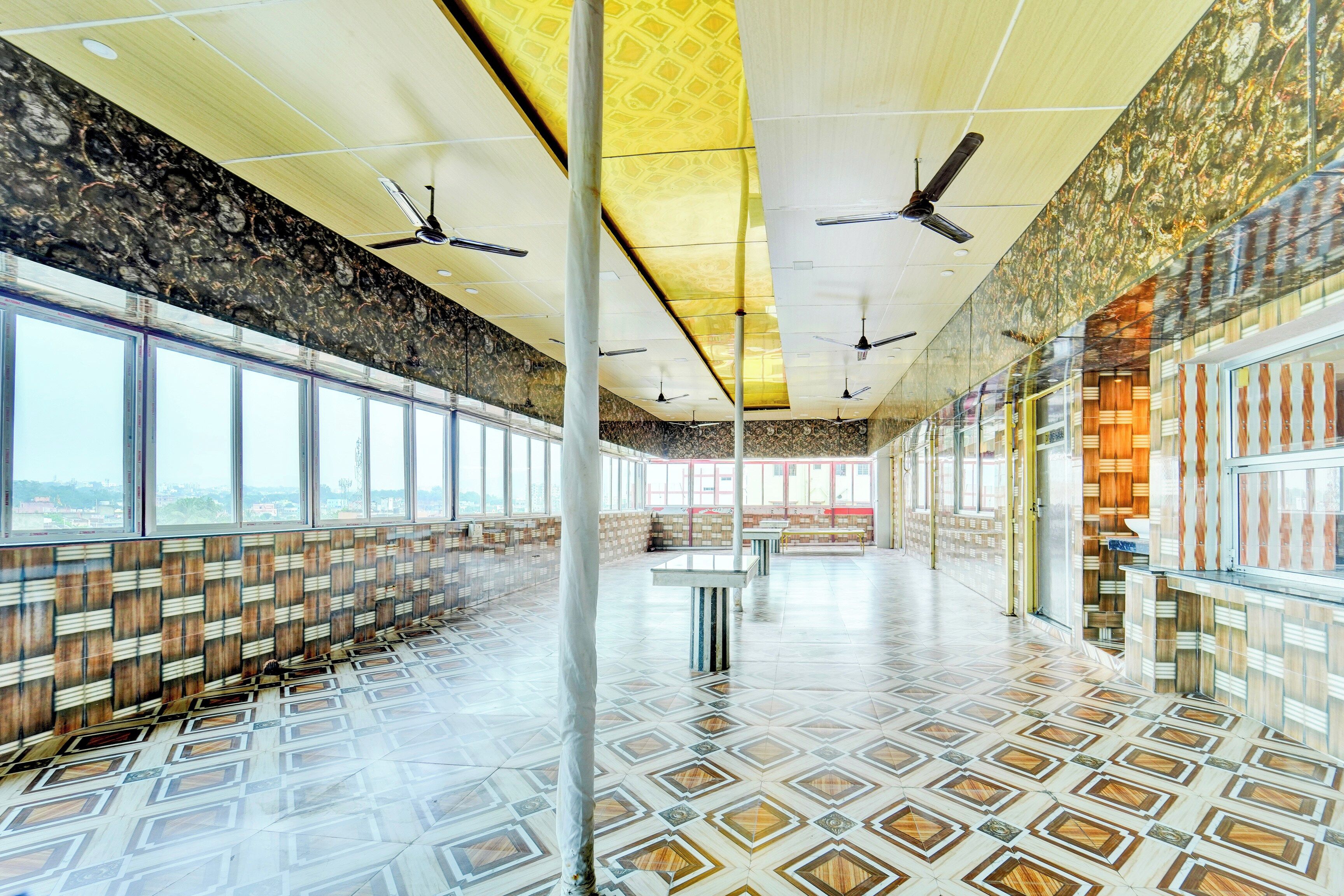 A spacious indoor area with a patterned floor, large windows, and ceiling fans.