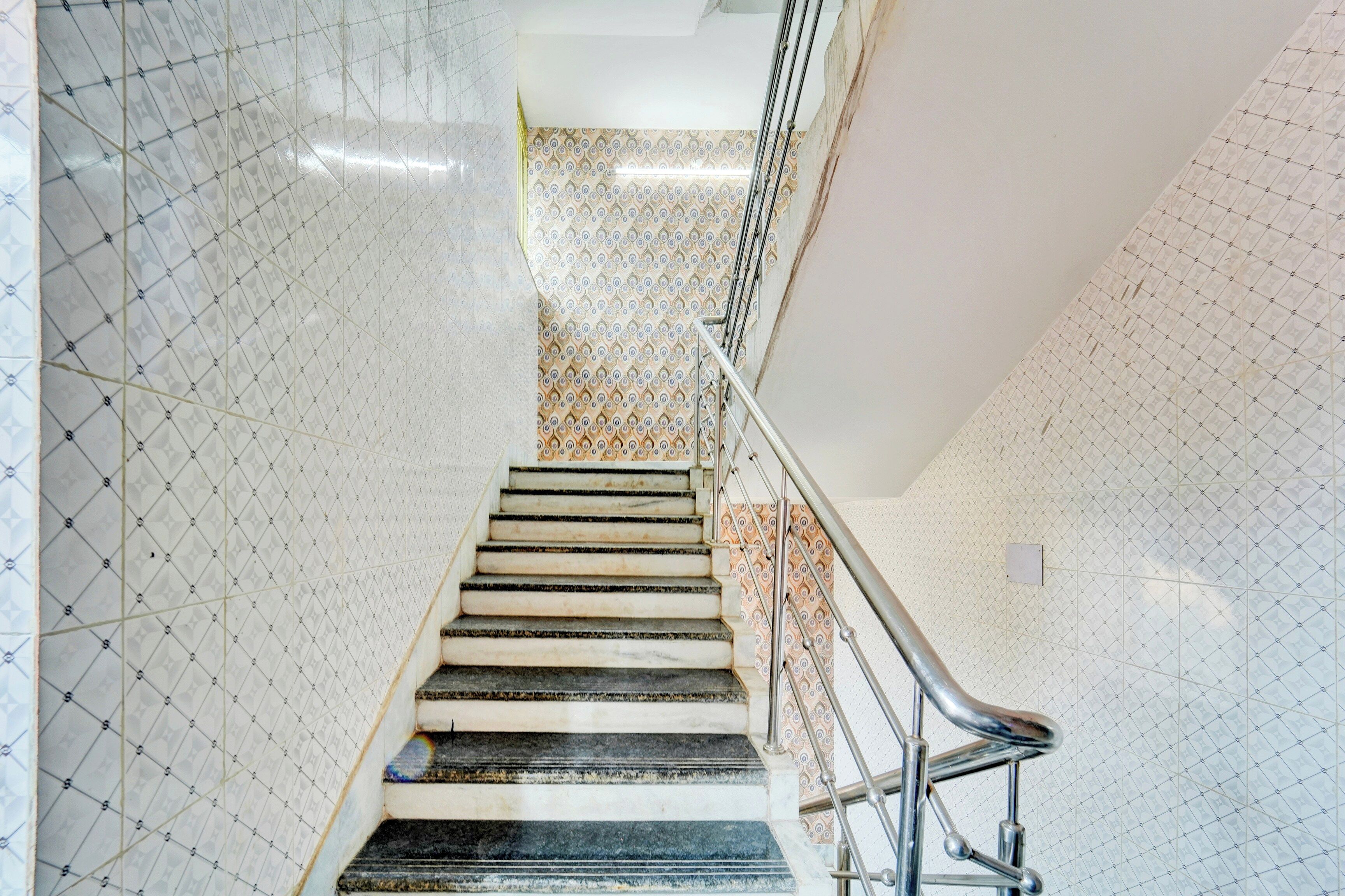 A staircase with a metal handrail, patterned walls, and a tiled floor.