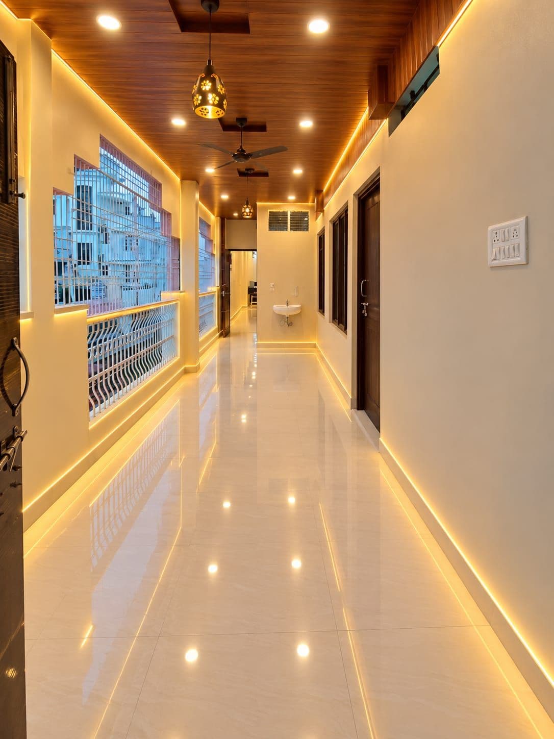 A corridor with a reflective floor, ceiling fans, pendant lighting, and a view of buildings through a window.