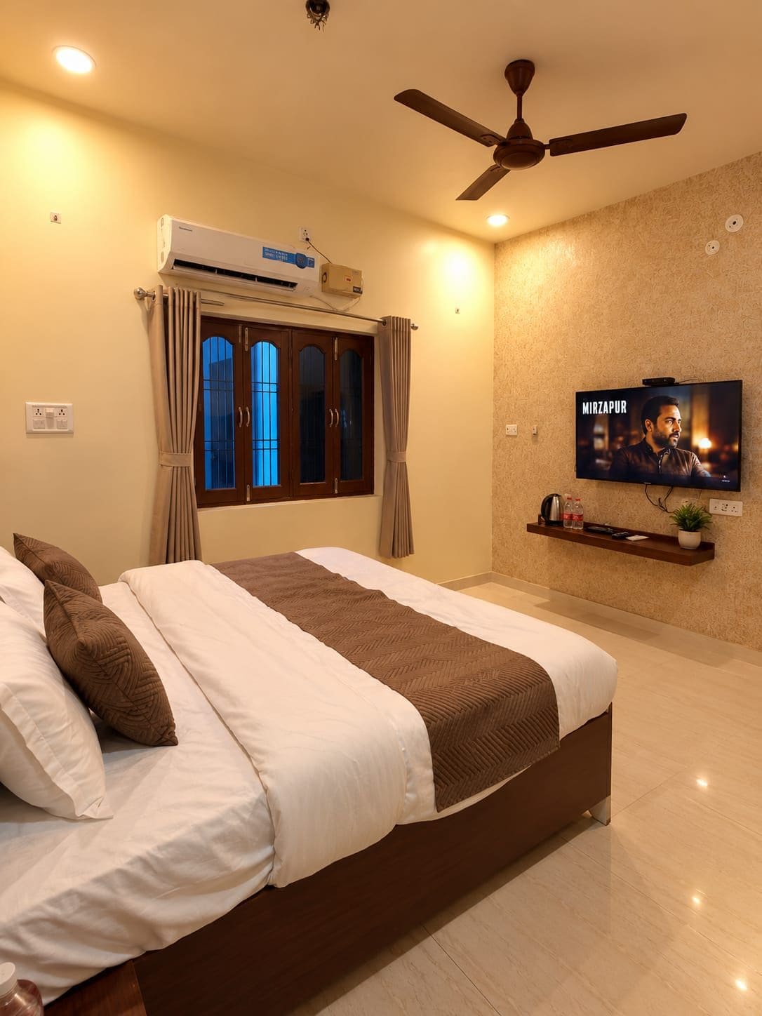 A hotel room with a bed, a ceiling fan, an air conditioning unit, a television, and a window with curtains.