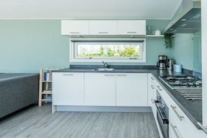 A compact kitchen with white cabinets, a window above the sink, and a built-in gas stove. - Holiday apartment 66 (Ellemeet)