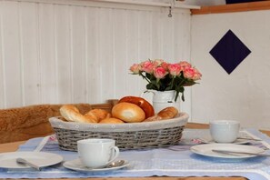 Een ontbijttafel met een broodmand, een bloevas en servies, kopjes en een karaf.