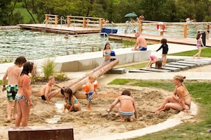 A pool area with a wooden deck, a sandy play area, and a water slide. - Tannenhof holiday and riding facility (Neukichen beim Heiligen Blut)