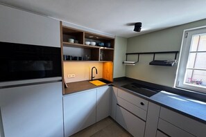 A compact kitchen with white cabinets, a black countertop, a built-in oven, and a window providing natural light. - Holiday home in Lindau with swimming pool (Lindau)
