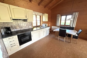 A compact kitchen with white cabinets, a stove, and a dining area with a table and chairs. - Country house Kreutzer "Beim Sima" (Rieden)