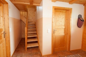 Eine Holztreppe führt zu einer zweiten Etage, eine Holztür mit Schuhablage und ein gefliester Boden.