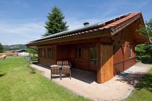 A wooden cabin with a covered patio, a dining area with chairs, and a view of the surrounding landscape. - Country house Kreutzer "Beim Sima" (Rieden)