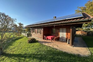 A wooden building with a covered patio, solar panels on the roof, and a table with chairs. - Country house Kreutzer "Beim Sima" (Rieden)