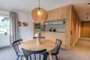 A modern kitchen with wooden cabinets, a round dining table with chairs, and a pendant light. - Holiday apartment with 1 bedroom (Oberstdorf)