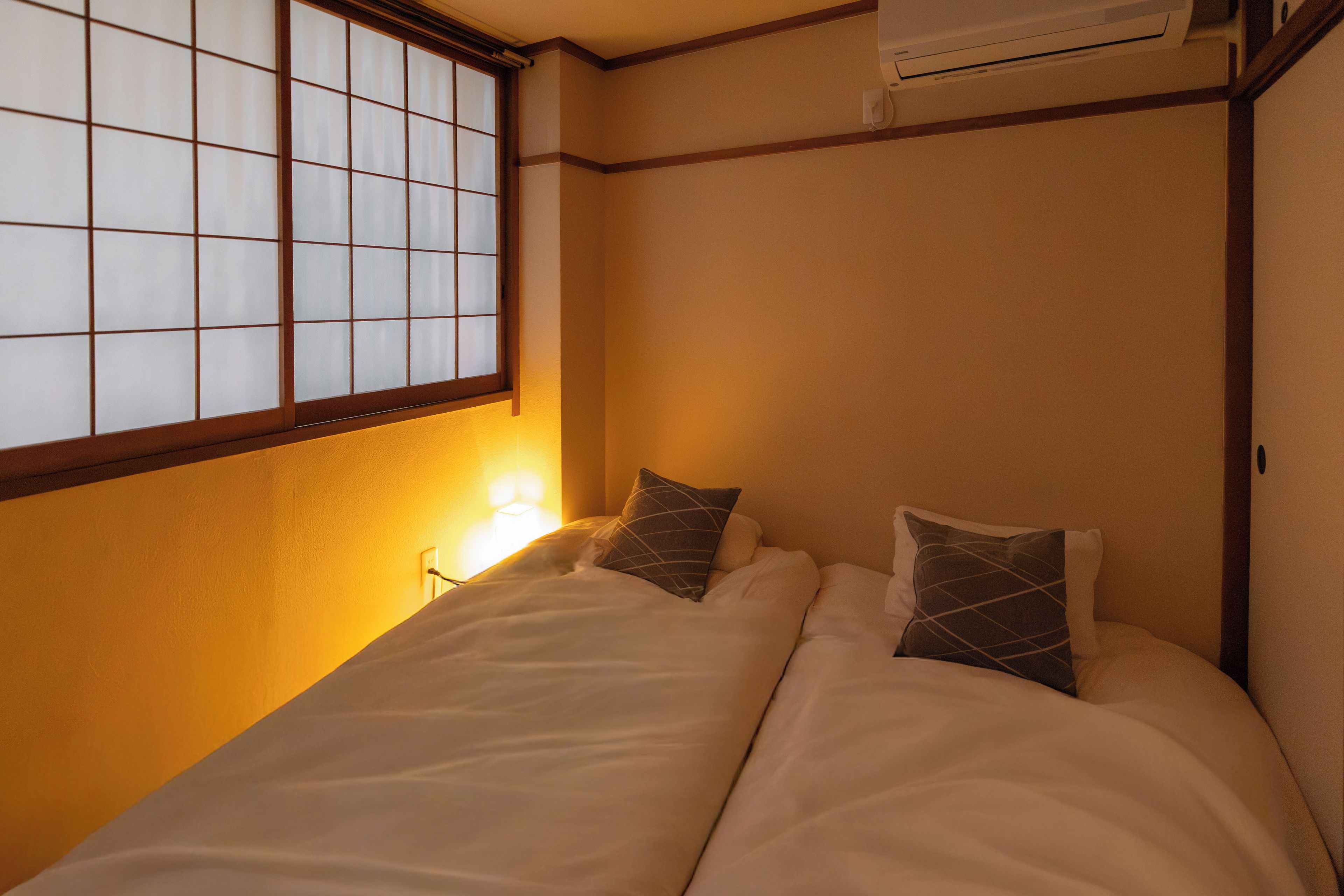A room with a bed, a window with a grid pattern, and an air conditioning unit.