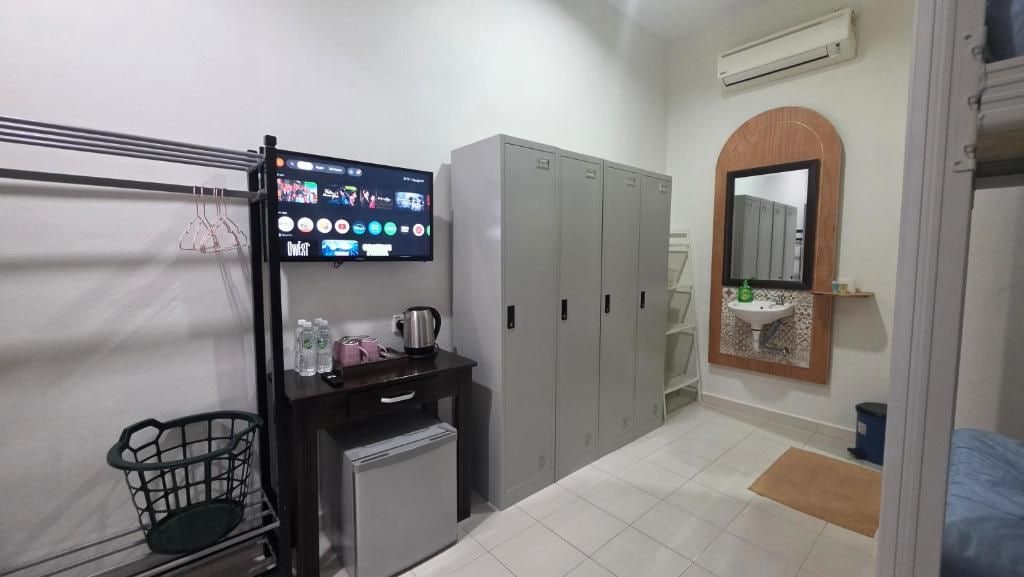 Habitación de hotel con televisión, armario, lavabo, espejo y un refrigerador pequeño.