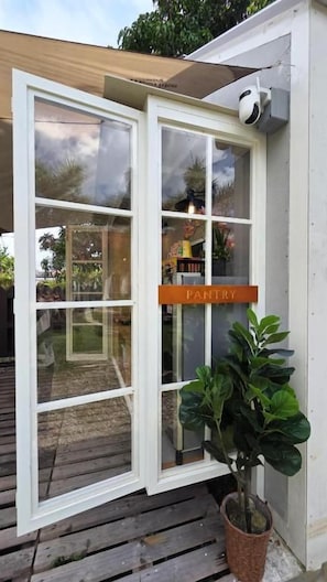 Una puerta con marco blanco, un letrero que dice 'PANTRY', una planta en maceta y una terraza de madera.