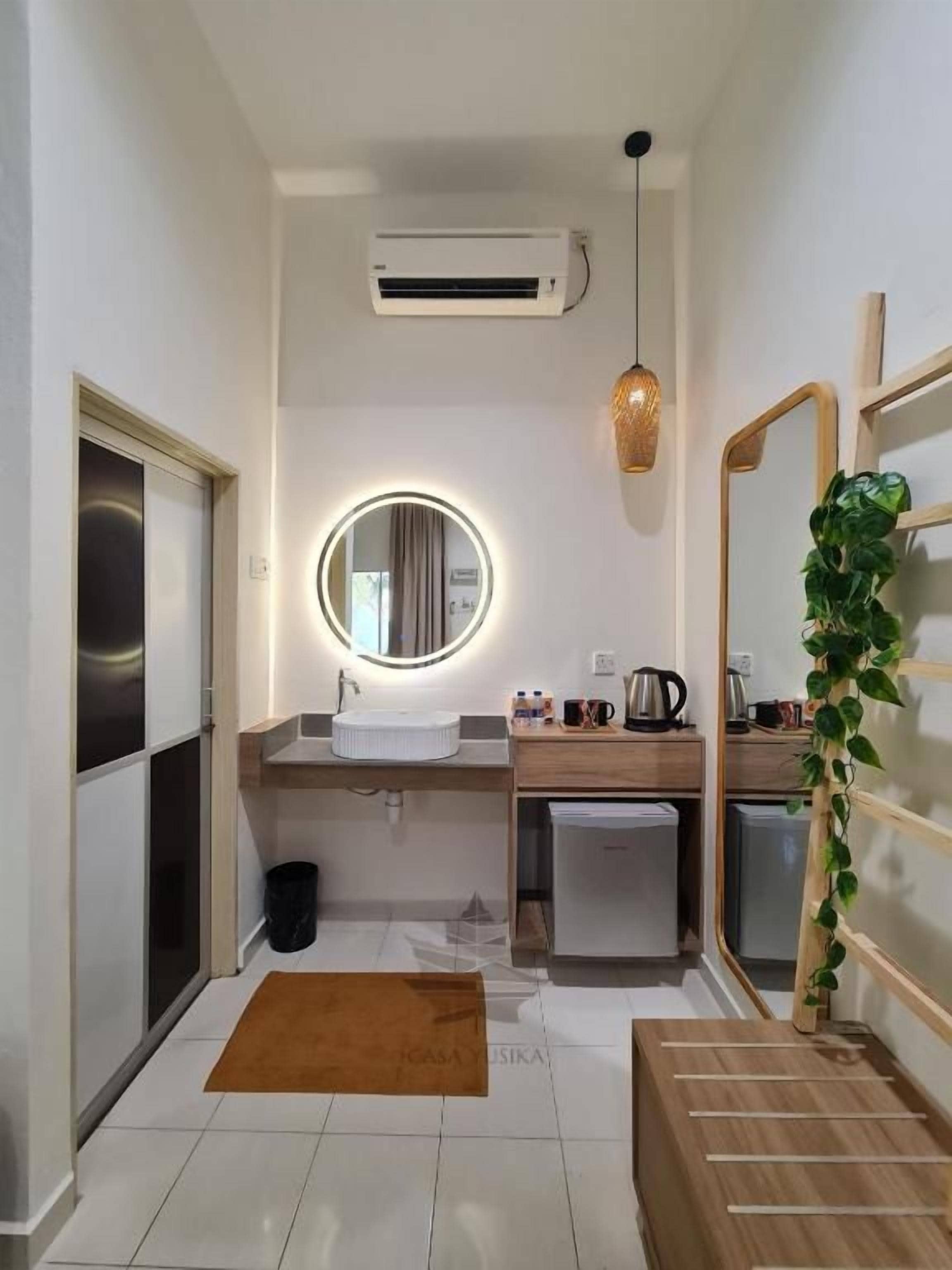 Un baño moderno con un espejo redondo, un lavabo, un armario pequeño y una planta.