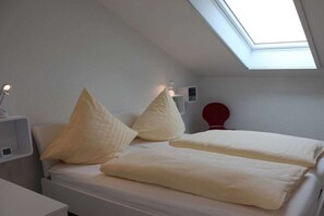 Ein Schlafzimmer mit Dachfenster, zwei Betten, einem Nachttisch und einem roten Gegenstand an der Wand.