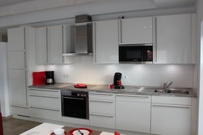 A modern kitchen with white cabinets, a black oven, a microwave, and a coffee maker. - Greetsieler Sonneneck (Greetsiel)