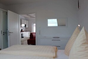 A bedroom with a bed, a bedside table, a mirror, and a red chair in the background. - Greetsieler Sonneneck (Greetsiel)