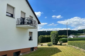A white building with a balcony, a well-maintained lawn, and a clear sky. - Eifelblick (Apartment Talblick) (Weinsheim)