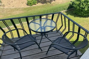A balcony with a glass table and two chairs, overlooking a grassy area. - Eifelblick (Apartment Talblick) (Weinsheim)
