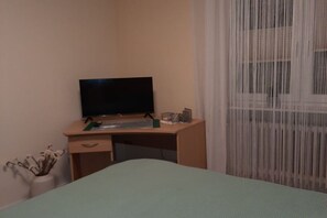 A hotel room with a bed, a desk with a television, and a window with sheer curtains. - Holiday apartment with 2 bedrooms (St. Wendel-Winterbach)