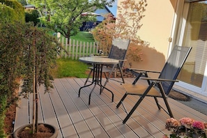 A wooden deck with a table and chairs, surrounded by greenery and a white fence. - Holiday apartment with 2 bedrooms (St. Wendel-Winterbach)
