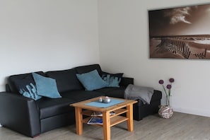 Ein Wohnzimmer mit einem schwarzen Sofa, einem Holztisch, einem gerahmten Bild an der Wand und einer Vase mit Blumen.