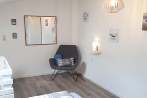 Et værelse med spejlvæg, en sort stol med puder, et natbord med lampe og en hvid kommode.