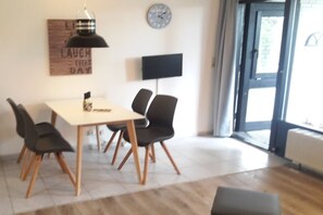 A dining area with a table and chairs, a clock, a flat-screen TV, and a door leading outside. - Holiday apartment with 2 bedrooms (Kellenhusen)