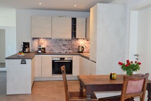 A modern kitchen with a built-in oven, a coffee machine, and a dining area with a table and chairs. - Holiday apartment in Wohlde with barbecue (Wohlde)