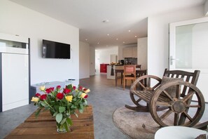 Uma sala de estar moderna com uma mesa de centro de madeira, uma TV de tela plana na parede e uma área de jantar com cadeiras e uma mesa de madeira.