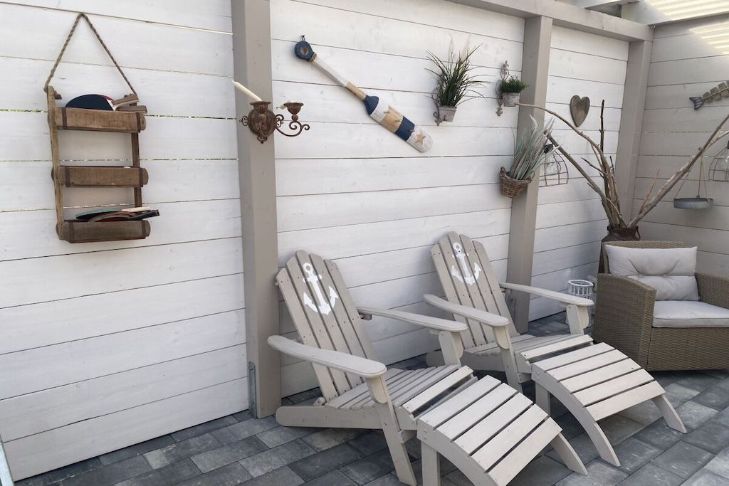 A patio area with Adirondack chairs, a small table, and decorative wall elements including a bat, a plant, and a heart-shaped decoration.