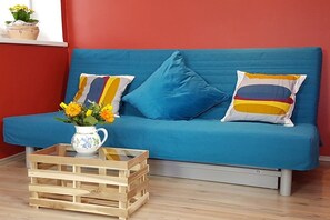 Ein blaues Sofa mit zwei Kissen, einer Holzkiste und einer weißen Krug mit Blumen.
