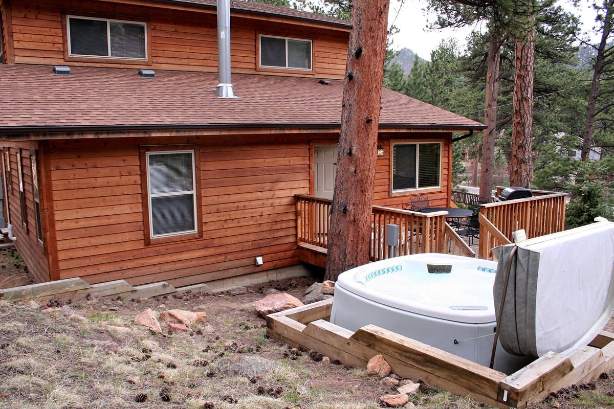 A two-story wooden cabin with a hot tub in the backyard.