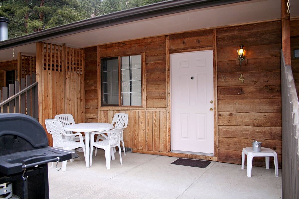 A wooden exterior with a white door, a small table with chairs, and a barbecue grill.